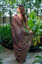 Woman in a patterned saree standing among green plants Green Kashmiri Kani Silk Saree