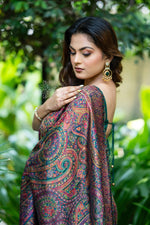 Woman in a patterned saree standing among green foliage Green Kani Pashmina Silk Saree
