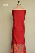 A red off-the-shoulder dress displayed on a mannequin, showing the back view with a decorative multicolor patterned hem against a plain beige background. Kani silk suit
