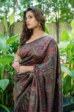 Woman wearing a patterned saree standing among green plants -Green Kani Jamawar Silk Saree