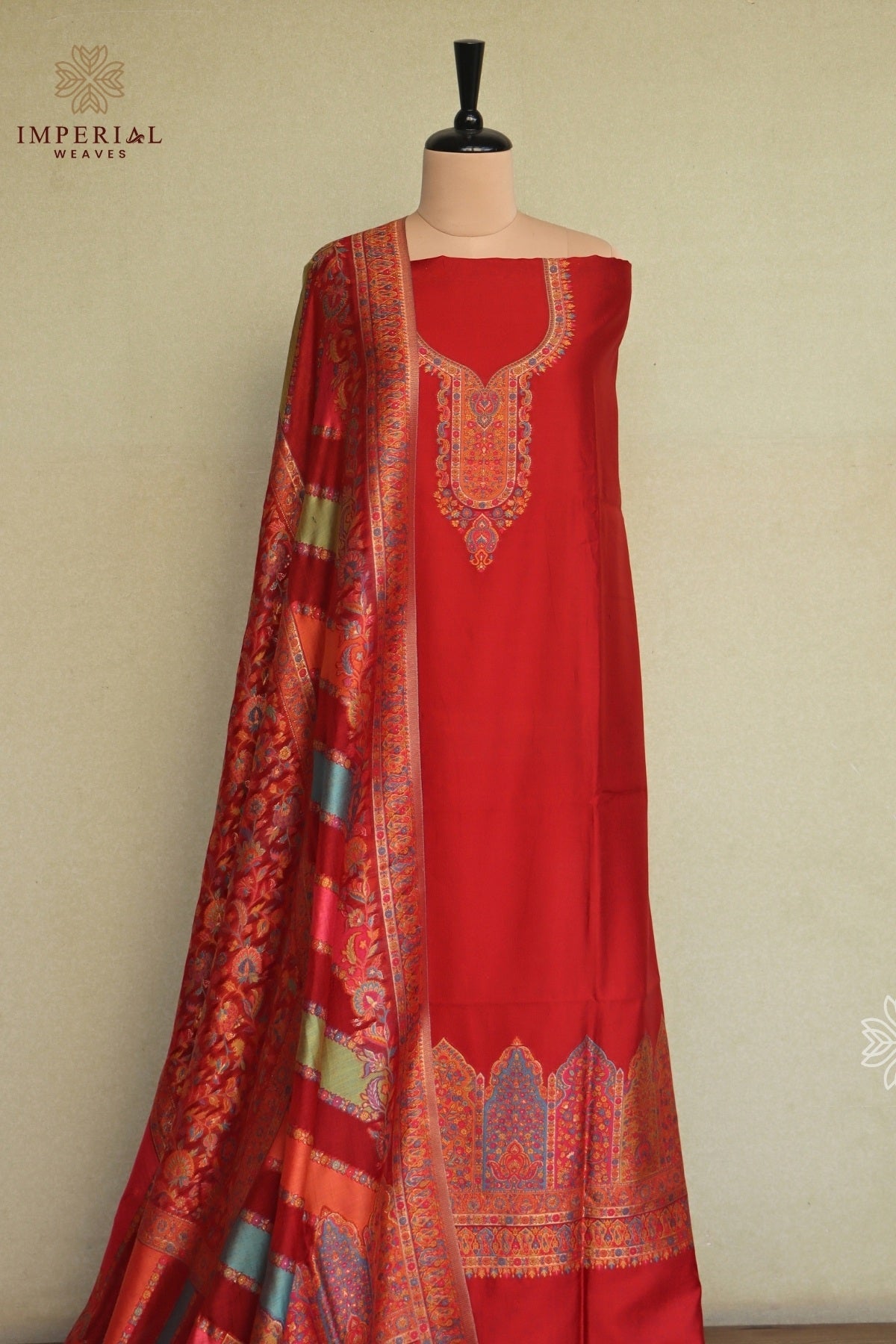 A red three-piece traditional Indian salwar suit set displayed on a mannequin, featuring a solid red kurta with an embroidered neckline, matching red trousers with a decorative hem, and a red dupatta with multicolor zari patterns. Kani silk suit