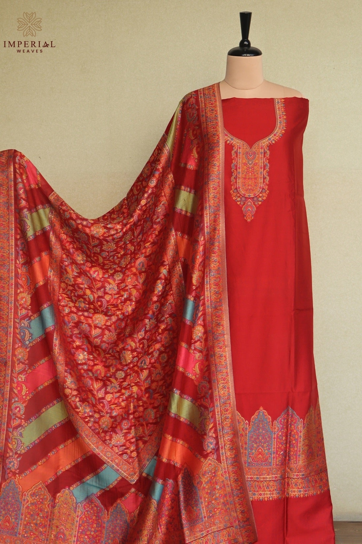 A red three-piece women's salwar suit set displayed on a mannequin, featuring a solid red kurta with ornate gold embroidery, a matching red salwar, and a highly patterned red dupatta with gold, green, and blue accents. Kashmiri Kani Suit 